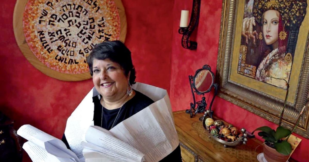 Genie Milgrom tenant des documents généalogiques et sa lignée matrilinéaire de Bnei Anousim devant une décoration hébraïque.
