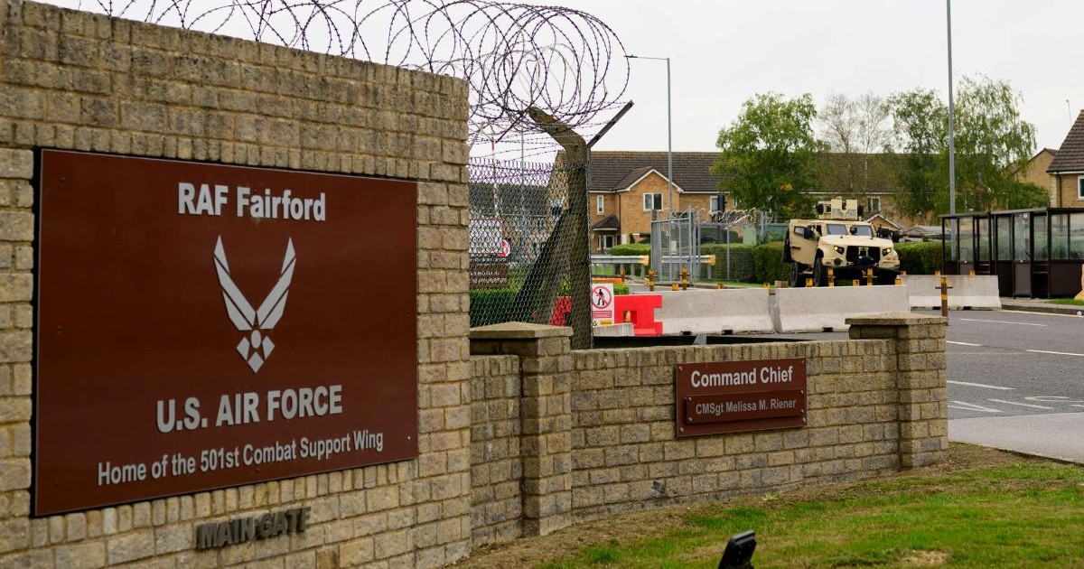 Entrée principale de la base militaire aérienne américaine de la RAF Fairford au Royaume-Uni avec barbelés, panneaux d'information et véhicule blindé.