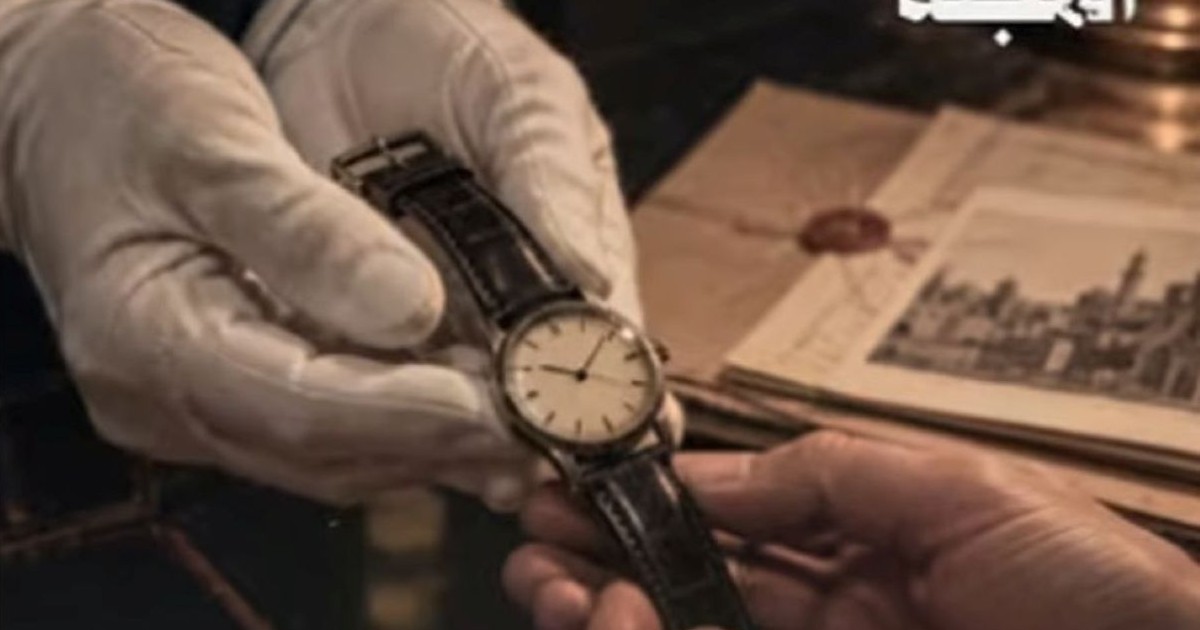 Gros plan sur la montre-bracelet d’Eli Cohen présentée entre deux mains, dont une gantée, avec des documents historiques en arrière-plan.