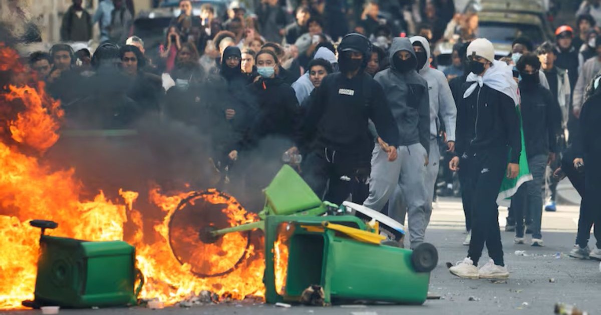Groupe de jeunes, dont plusieurs masqués, dans une rue en France, près de poubelles et d'objets en feu lors de violences urbaines.