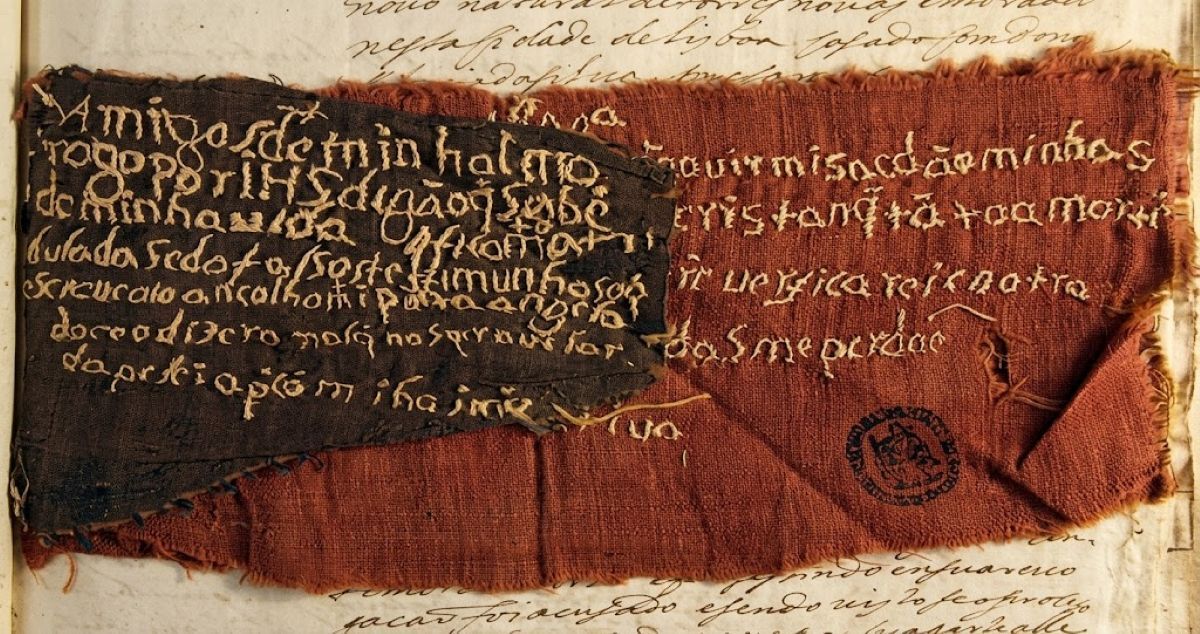 L'image montre des fragments de tissu rouge et sombre brodés ou écrits à la main, conservés comme pièces à conviction dans les dossiers du Tribunal du Santo Ofício aux Arquivo Nacional Torre do Tombo à Lisbonne.