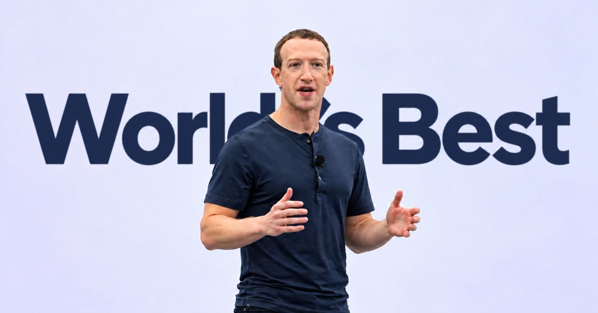 Mark Zuckerberg en tee-shirt bleu foncé, les mains ouvertes pendant une prise de parole, sur fond clair.