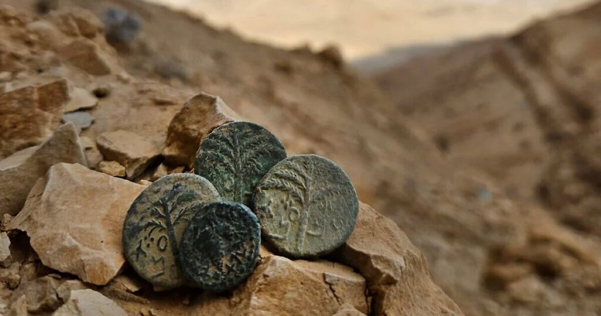 Quatre pièces de monnaie antiques en bronze datant de la révolte de Bar Kokhba, posées sur des rochers dans le désert de Judée.
