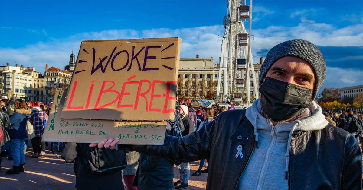 Manifestant masqué tenant une pancarte « Woke Libérée » au milieu d’un rassemblement