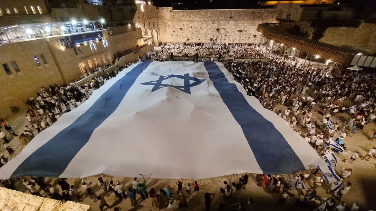 Une foule devant le Kotel recouverte par un immense drapeau israélien