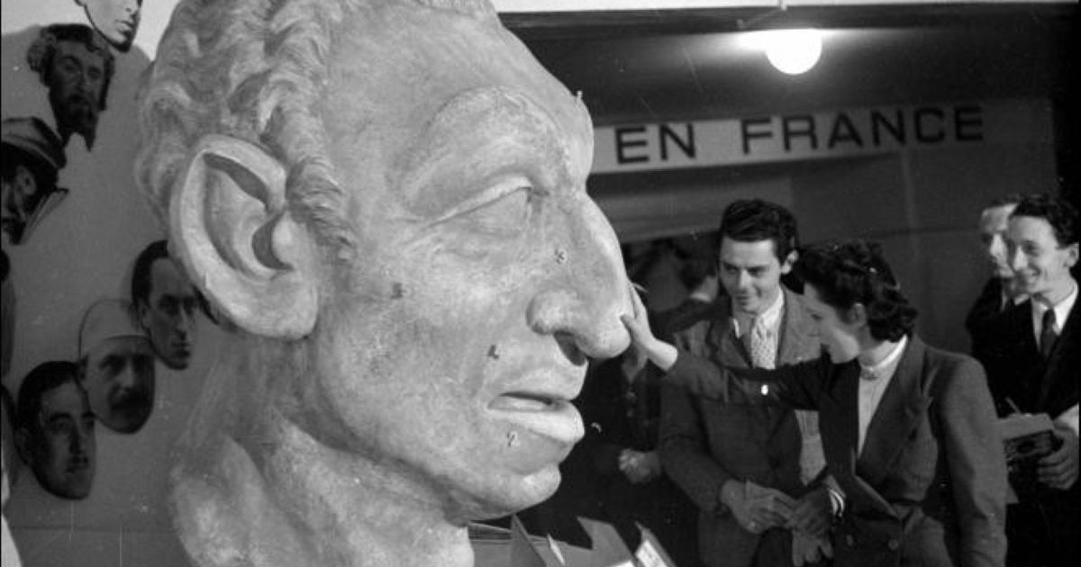 Cette photographie montre une visiteuse touchant le nez d'un grand buste caricatural présentant des stéréotypes antisémites.