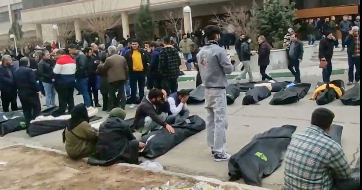 Image d'archive montrant des proches en deuil rassemblés autour de corps enveloppés dans des housses mortuaires suite à la répression sanglante en Iran.