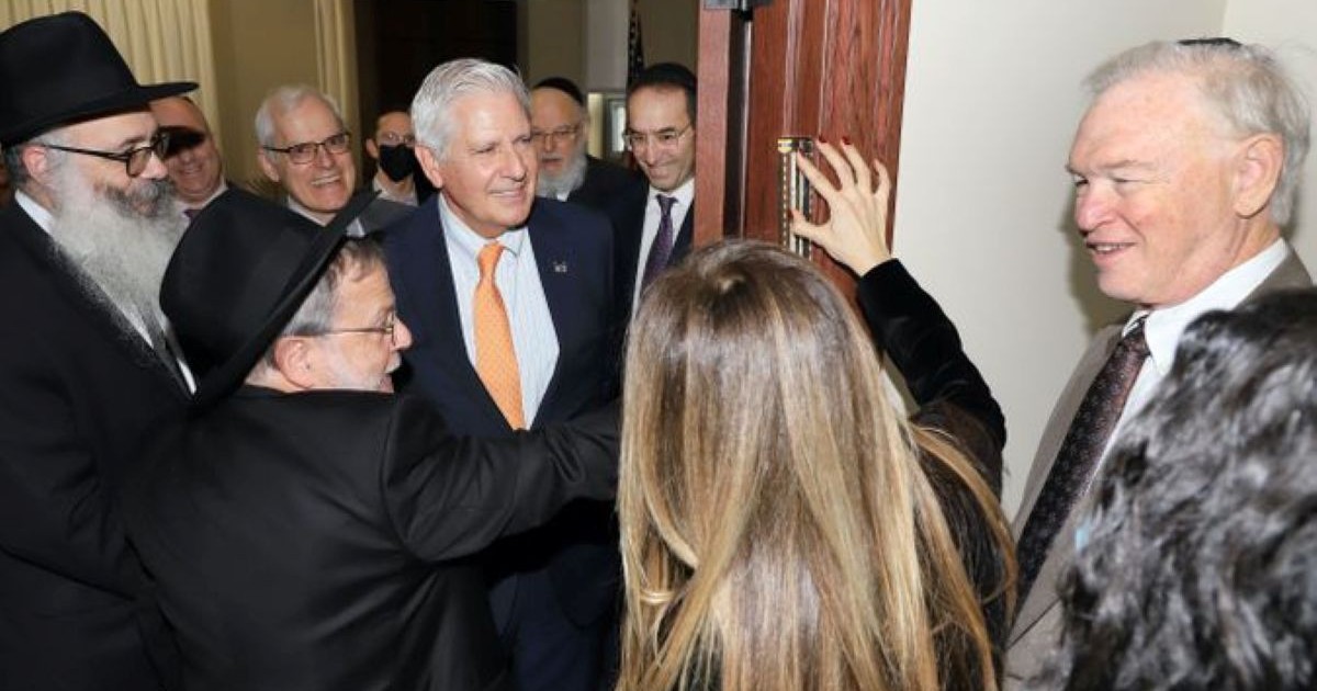 L'exécutif du comté de Nassau, Bruce Blakeman, entouré de rabbins et de dignitaires, assiste à la fixation d'une mezouza sur le montant de la porte de son bureau lors d'une cérémonie.