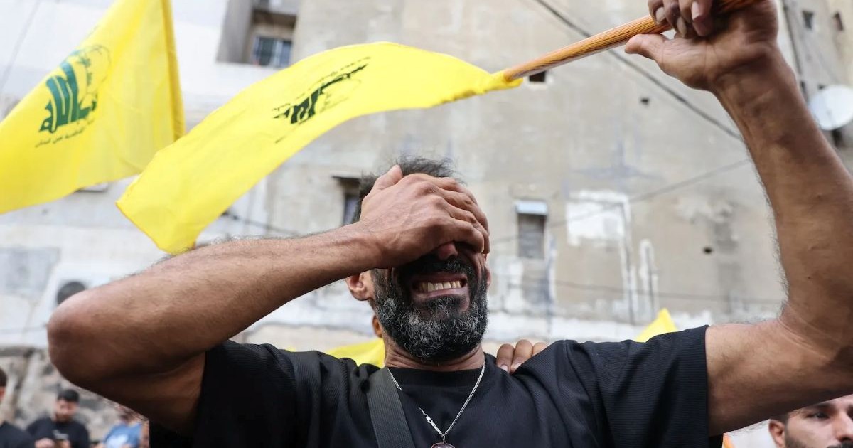 Un partisan du Hezbollah en pleurs cachant son visage sous des drapeaux jaunes, illustrant la détresse du mouvement après l'attaque des beepers