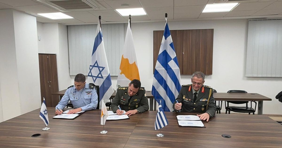 Responsables militaires israélien, grec et chypriote signant un accord de coopération sous les drapeaux des trois pays.