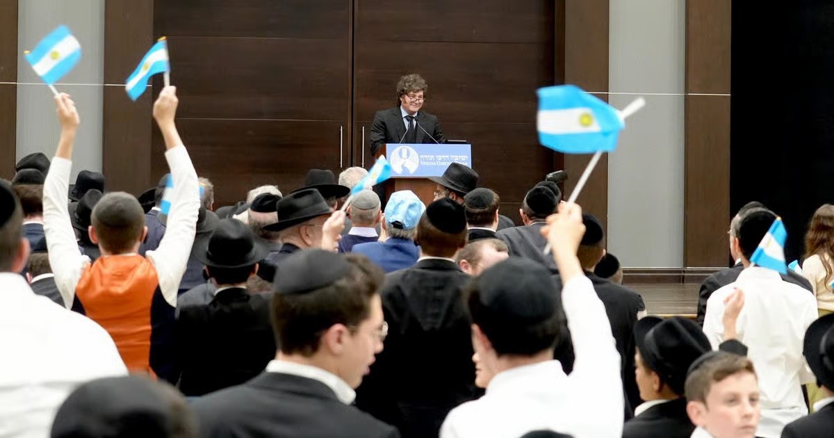 Javier Milei s'exprimant à la yeshiva Darchei Torah devant un public agitant des drapeaux de l'Argentine.