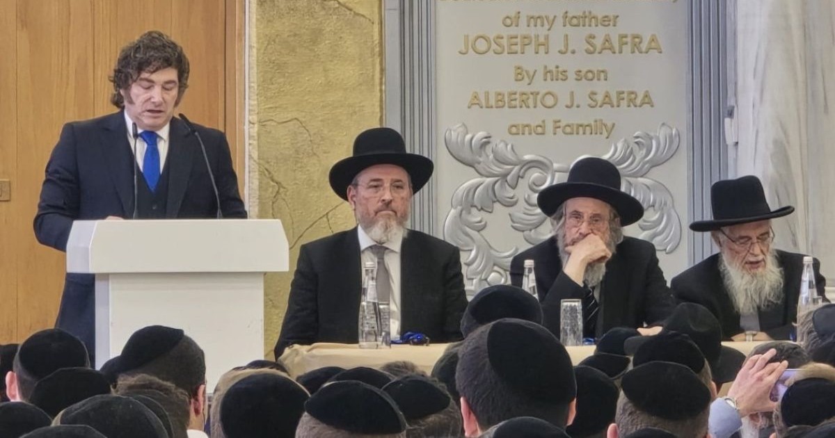 Javier Milei prononçant un discours derrière un pupitre lors de sa visite, aux côtés de personnalités rabbiniques, devant un public assis
