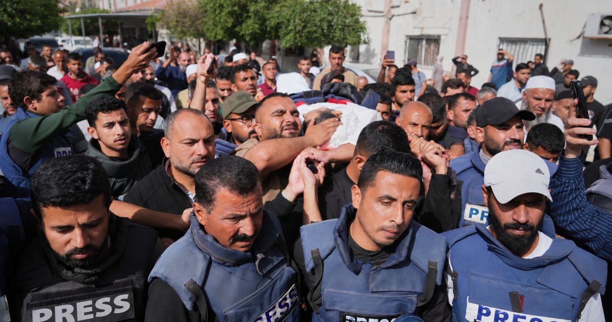 Des hommes portant des gilets PRESS au premier plan d’un cortège funéraire