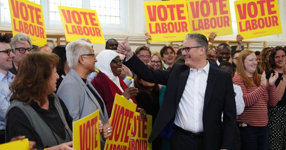 Le Premier ministre britannique Keir Starmer souriant et levant le pouce lors d'un meeting politique du parti Labour, entouré de militants.