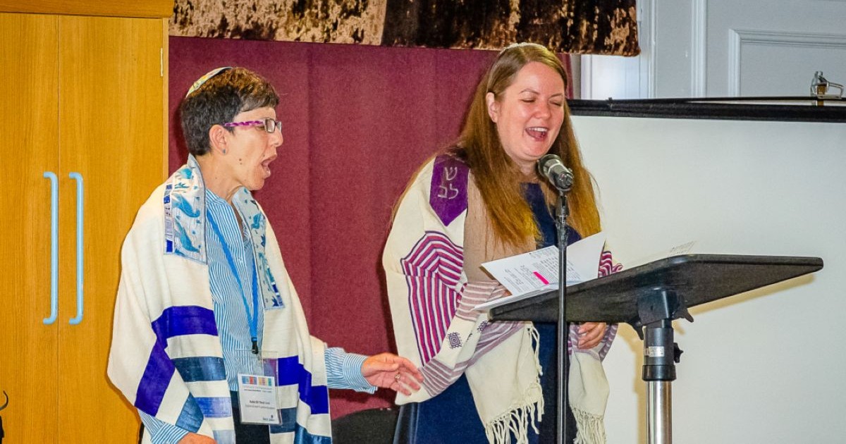 Deux femmes rabbines portant un talit prient et chantent ensemble devant un pupitre lors d'un office de Liberal Judaism.