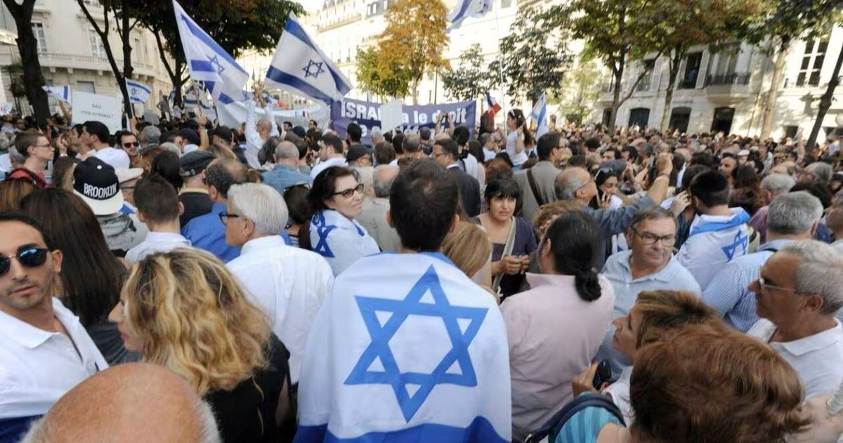 Foule participant à un rassemblement de soutien à Israël dans une rue, avec de nombreux drapeaux israéliens et une étoile de David visible au premier plan.