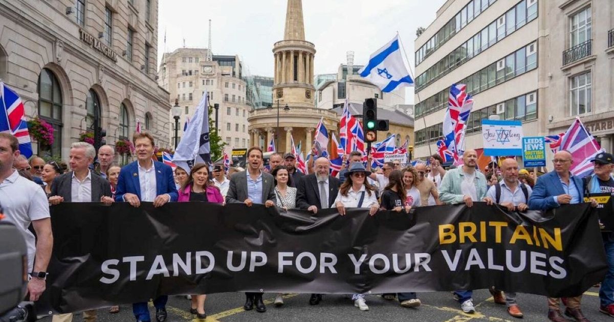 Manifestants à Londres derrière une banderole appelant les Britanniques à défendre leurs valeurs, avec des drapeaux britanniques et israéliens.