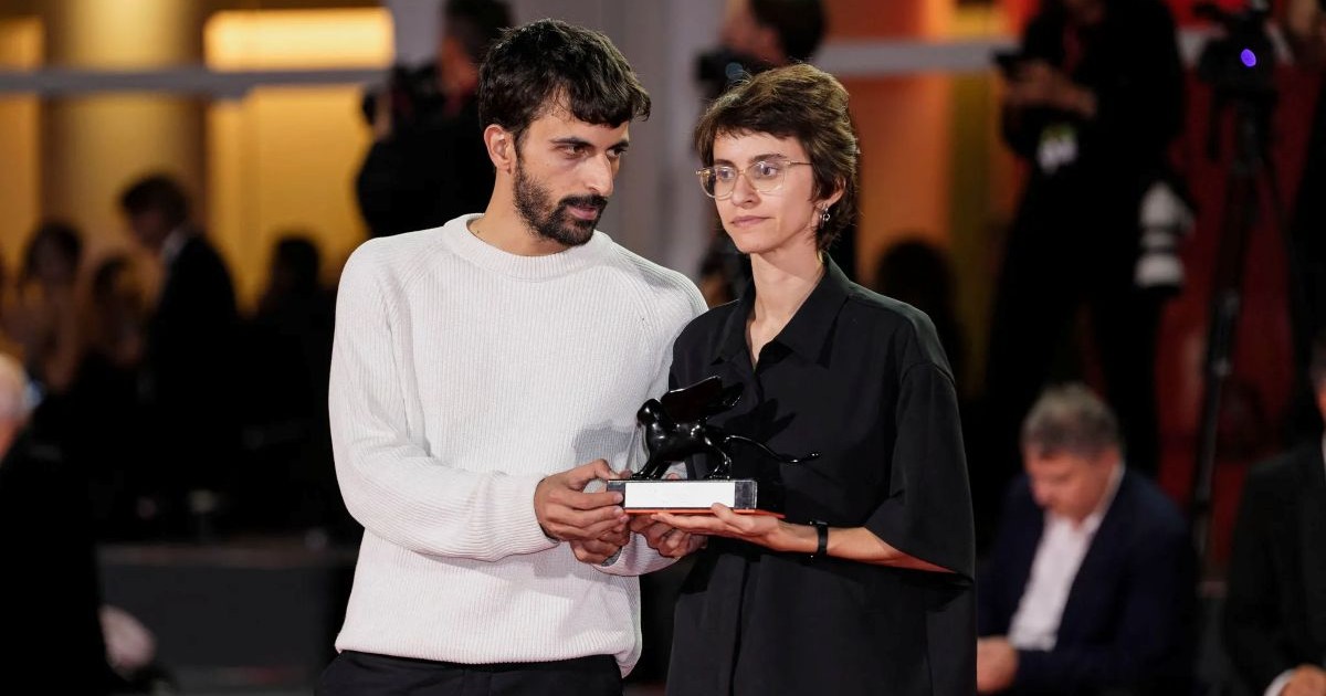 Youval Avraham et Rachel Szor tenant ensemble une statuette de lion noir sur un socle, lors d'une cérémonie officielle sur fond de tapis rouge.