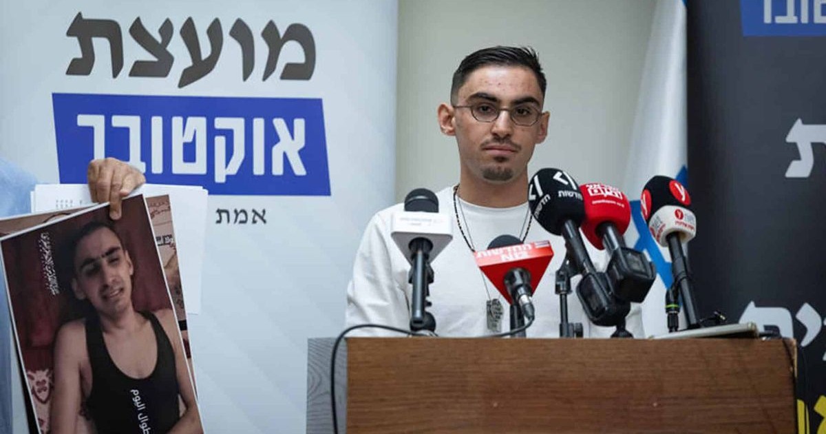 Rom Braslavski, ancien otage, lors d'une conférence de presse à la Knesset, avec une pancarte en hébreu et une photo d'otage en arrière-plan.